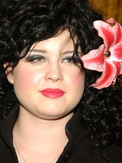 Kelly Osbourne con melena ondulada negra y tocado de flor